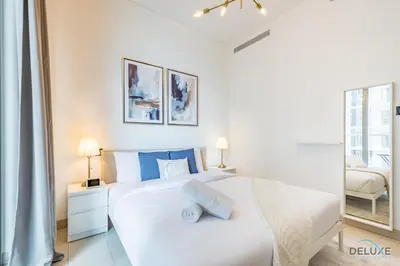 a white bedroom with a large white bed with blue pillows at Charming 1BR Apartment in Sobha Creek Vistas Reserve, Al Merkadh by Deluxe Holiday Homes in Dubai