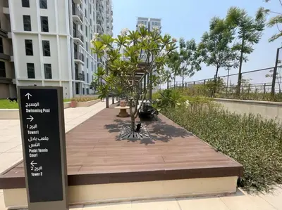 a boardwalk with trees and a sign in front of a building at Luxury at Socio Dubai Hills, 2 Beds, Sleeps 4 - DVH Holiday Homes in Dubai