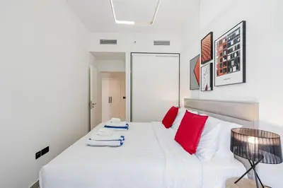 a bedroom with a white bed with red pillows at Luxury at Socio Dubai Hills, 2 Beds, Sleeps 4 - DVH Holiday Homes in Dubai