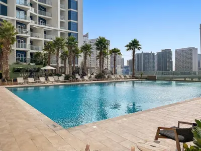 a large swimming pool with palm trees and buildings at A Living-Modern Studio Apartment with Balcony & Canal view at Prive 2507B ,Business Bay in Dubai