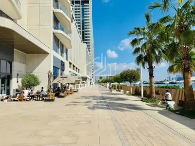 a sidewalk with palm trees and people sitting at tables at Stunning 2 Bedroom in Emaar Beachfront in Dubai