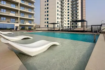 a swimming pool with white sculptures in front of buildings at Waves - Stylish 1BR Close to IMG World & Global Village in Dubai