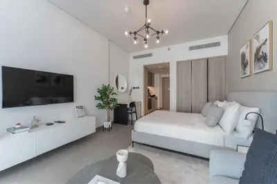 a white bedroom with a bed and a tv at HAVN - Smart Home Studio in Oxford Terraces, JVC in Dubai