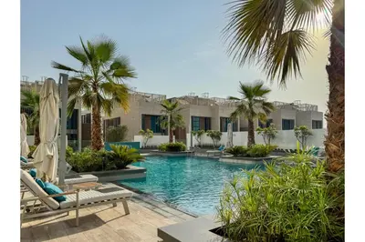 a swimming pool with palm trees in front of a building at HAVN - Smart Home Studio in Oxford Terraces, JVC in Dubai