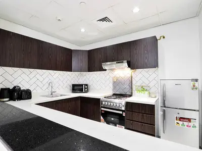 a kitchen with wooden cabinets and a white refrigerator at StoneTree - Fully Furnished - Dania 2 in Dubai