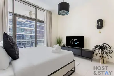 a white bedroom with a bed and a tv at Calm and Cozy Studio in Loreto 1A, Damac Hills in Dubai