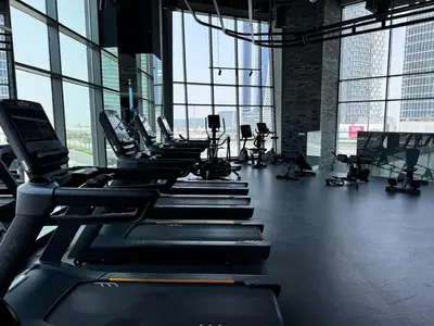 a gym with rows of tread machines in a room with windows at 1 Bedroom with Canal View - 15 Northside in Dubai