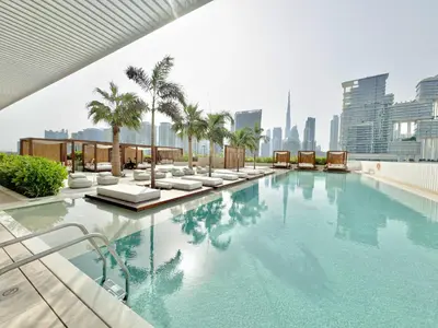 a swimming pool with chairs and palm trees on a building at Business-Ready Executive Studio with Burj View in Dubai
