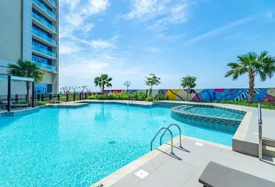a large swimming pool with palm trees and a building at Cozy High-Floor Studio with Amazing Views in Dubai