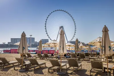 a beach with chairs and a ferris wheel in the background at Stylish 2BR Apt just minutes from Beach in Dubai