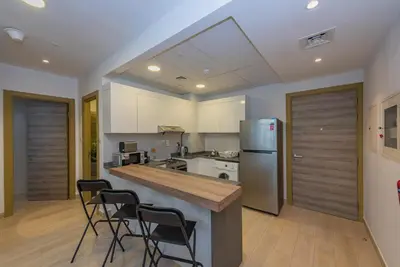 a kitchen with a counter and a refrigerator and chairs at Bloom Heights 1 BR, JVC in Dubai