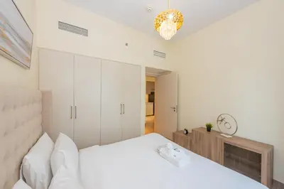 a white bedroom with a large bed and a chandelier at Park Heights 1 BR, Dubai Hills in Dubai
