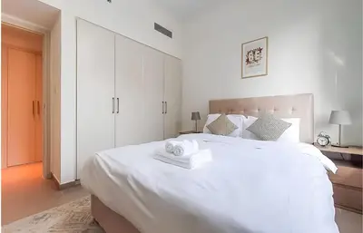 a white bedroom with a large white bed with two towels at Park Heights, Dubai Hills- Cozy 1-BR in Dubai