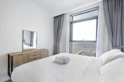 a bedroom with a white bed with a mirror and a window at Fully Equipped 1BR with Private Beach Access in Dubai