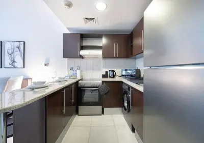 a kitchen with a stainless steel refrigerator and wooden cabinets at Lux Studio in JLT with Amazing View Next to the Metro - Dubai Arch tower in Dubai