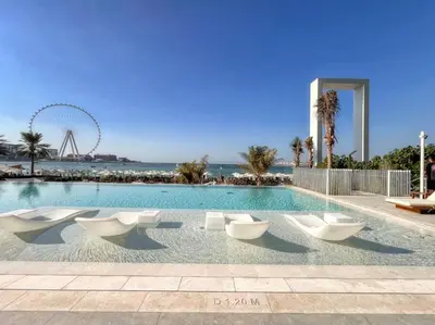 a swimming pool with white chairs and a ferris wheel at Panoramic Sea View 2BR in JBR in Dubai