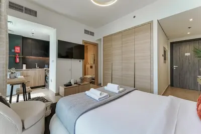a bedroom with a large white bed and a kitchen at Stylish Studio with Gym & Pool Access in Dubai