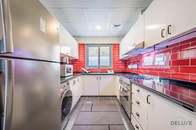 a large kitchen with white cabinets and red tiles at Charming 3BR Townhouse with Study Room in Damac Hills 2 Centaury, Dubailand By Deluxe Holiday Homes in Dubai