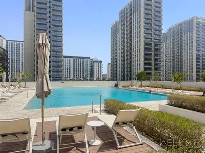 a pool with chairs and an umbrella and some buildings at WelHome - Beautiful 1BR Apt in Dubai Hills with City View in Dubai