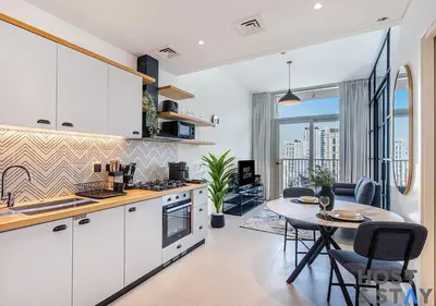 a kitchen with white cabinets and a table and a dining room at Modern 1bed Haven in Dubai Hills in Dubai