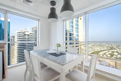 a white dining room with a white table and chairs and large windows at GuestReady - Home away from home in JLT in Dubai