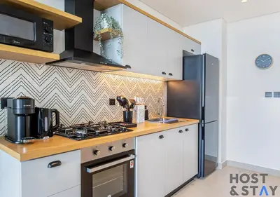 a kitchen with white cabinets and a stove top oven at Lux 1BR Near Dubai Hills Mall in Dubai