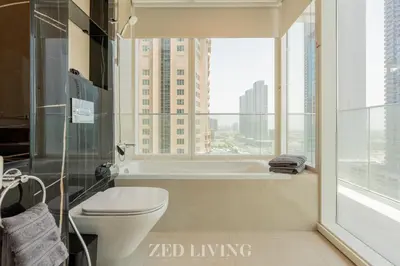 a bathroom with a tub and a toilet and a window at Me Do Re - Luxury Living 1 BR with Panoramic View - Zed Living in Dubai
