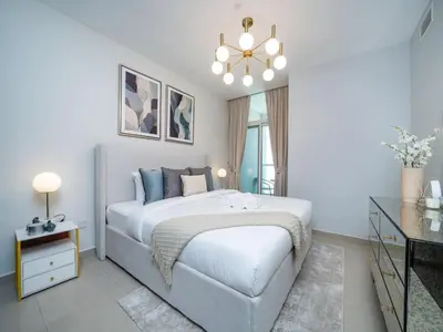 a white bedroom with a bed and a chandelier at Sleek 2 Bed in Sports City in Dubai