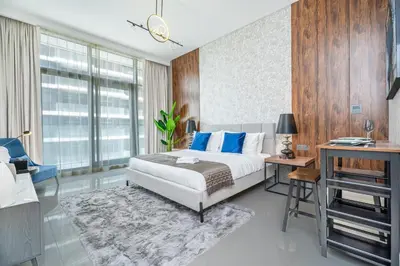 a bedroom with a bed with blue pillows and a desk at Escape24 Premium Studio in Damac Hills in Dubai