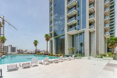 a swimming pool with lounge chairs and a building at Stylish 1BR in JVC with Pool & Nearby Parks in Dubai