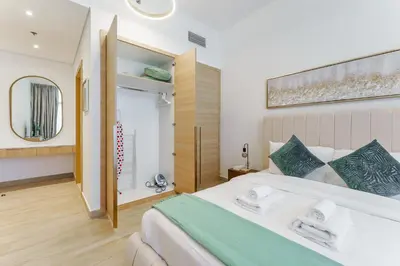 a bedroom with a large white bed and a mirror at Stylish 1BR in JVC with Pool & Nearby Parks in Dubai