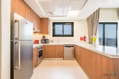 a kitchen with wooden cabinets and a stainless steel refrigerator at Captivating 1BR Apartment in Zazen Gardens, Al Furjan by Deluxe Holiday Homes in Dubai
