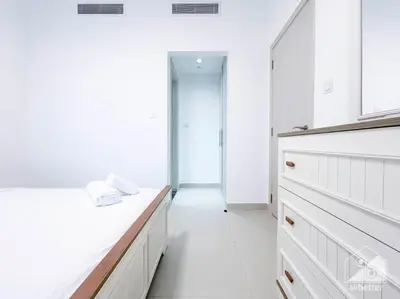 a white kitchen with white cabinets and a hallway at Luxurious 1BR Apt with Balcony in Production City in Dubai
