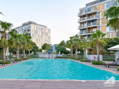 a large swimming pool with palm trees and a building at Luxurious 1BR Apt with Balcony in Production City in Dubai
