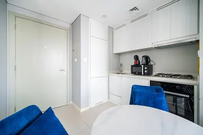a kitchen with white cabinets and a table and blue chairs at Elegant Escapes - Lavish 1B,Dubai Water Canal View in Dubai