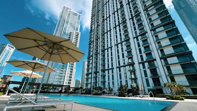 a pool in front of a tall building with two umbrellas at Luxury High Floor Apartment with Downtown Boulevard View Opposite Dubai Mall in Dubai
