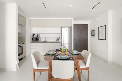 a white kitchen with a wooden table and chairs at Silkhaus 1BDR in Marina Vista with Private Beach in Dubai