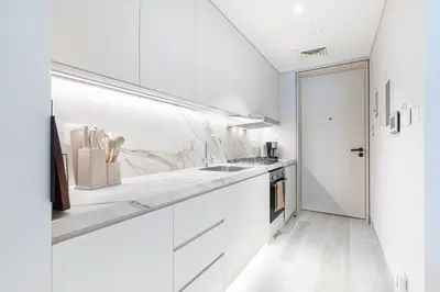 a white kitchen with white cabinets and a sink at Luxe Central Marina Studio with Rooftop Pool in Dubai