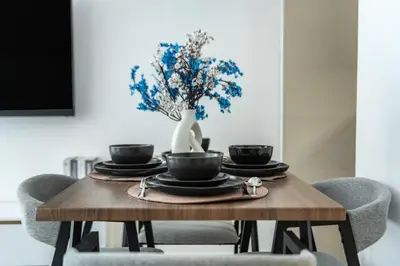 a dining room table with chairs and a vase with blue flowers at ShoresInn - Chic Waterfront Living in Dubai Marina in Dubai