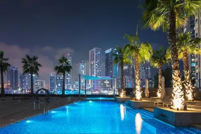 a pool with palm trees and a city at night at Sparkle Tower Panoramic Marina View 1BR in Dubai