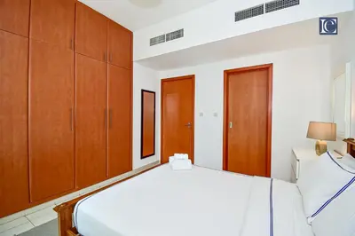 a bedroom with a white bed and wooden cabinets at Luxury Escapes - Spacious 1BR with Pool view - Ghozlan 2 The Greens in Dubai