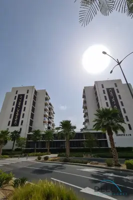two tall buildings with palm trees in front of a street at Premium 1BR at DAMAC Hills Loreto 1B in Dubailand by Deluxe Holiday Homes in Dubai