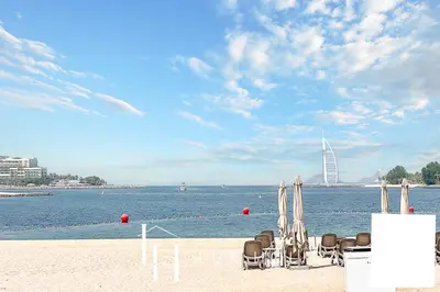 a group of chairs and umbrellas on a beach at LUX The Shoreline Palm Island Penthouse in Dubai