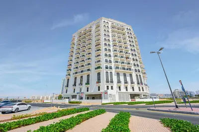 a tall white building with a car parked in front of it at Comfortable Studio With Dubailand Vibes in Dubai