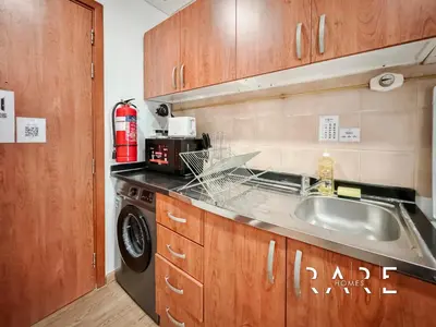 a kitchen with a sink and a washing machine at Rare Holiday Homes - Near City Center Ma'eisem - Pool view - Crescent Tower A - R706 - IMPZ in Dubai