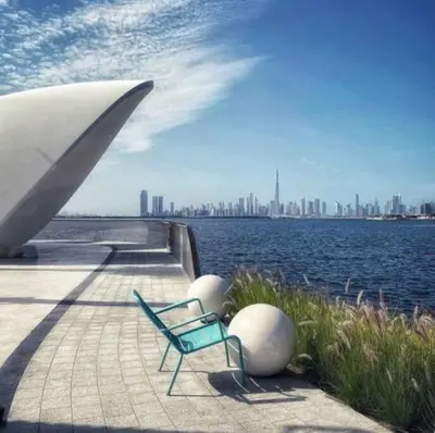 a green chair sitting on a boardwalk next to a body of water at Contemporary 1BR condo with pool at Creek Harbour in Dubai