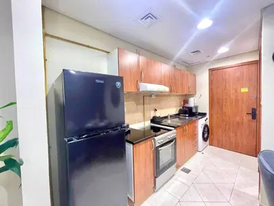 a kitchen with a black refrigerator and wooden cabinets at Amazing Studio Apartment in The Crescent A Tower IMPZ in Dubai