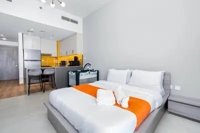a large white bed in a room with a kitchen at Cozy Studio - Dubai Land -Tiger V Tower in Dubai