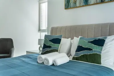 a bed with a blue comforter and pillows with two rolled towels at ShoresInn - Radiant 1BR in Dubai Marina in Dubai