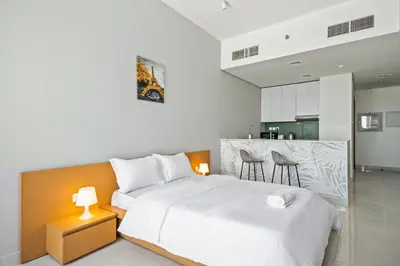 a bedroom with a white bed and a kitchen at Bright Studio In Vibrant Dubailand District in Dubai